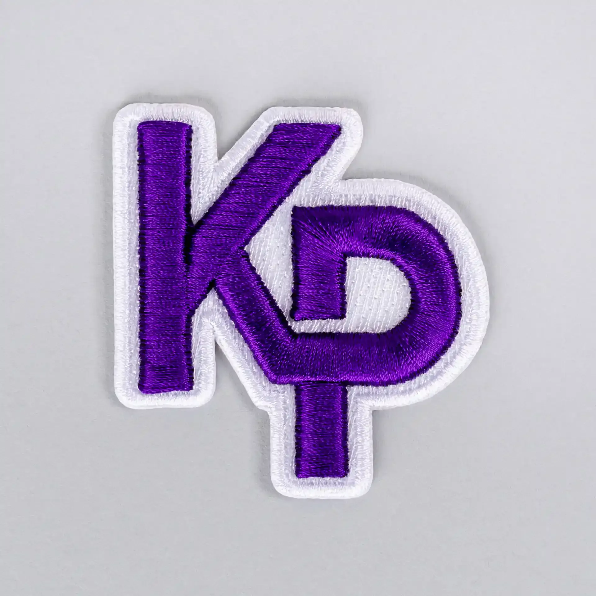 Purple and white interlocking KP monogram logo using 3D puff embroidery digitizing by Sassy Digitizing.
